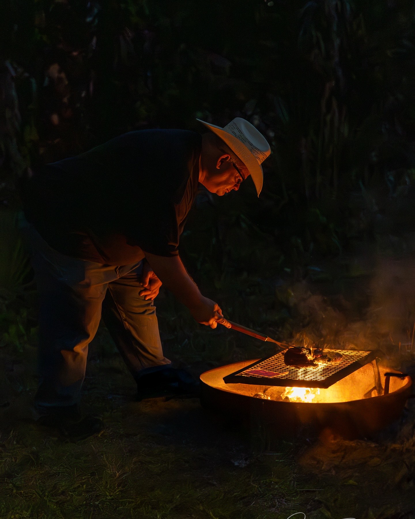 Camp cook grilling dinner over an open fire at night