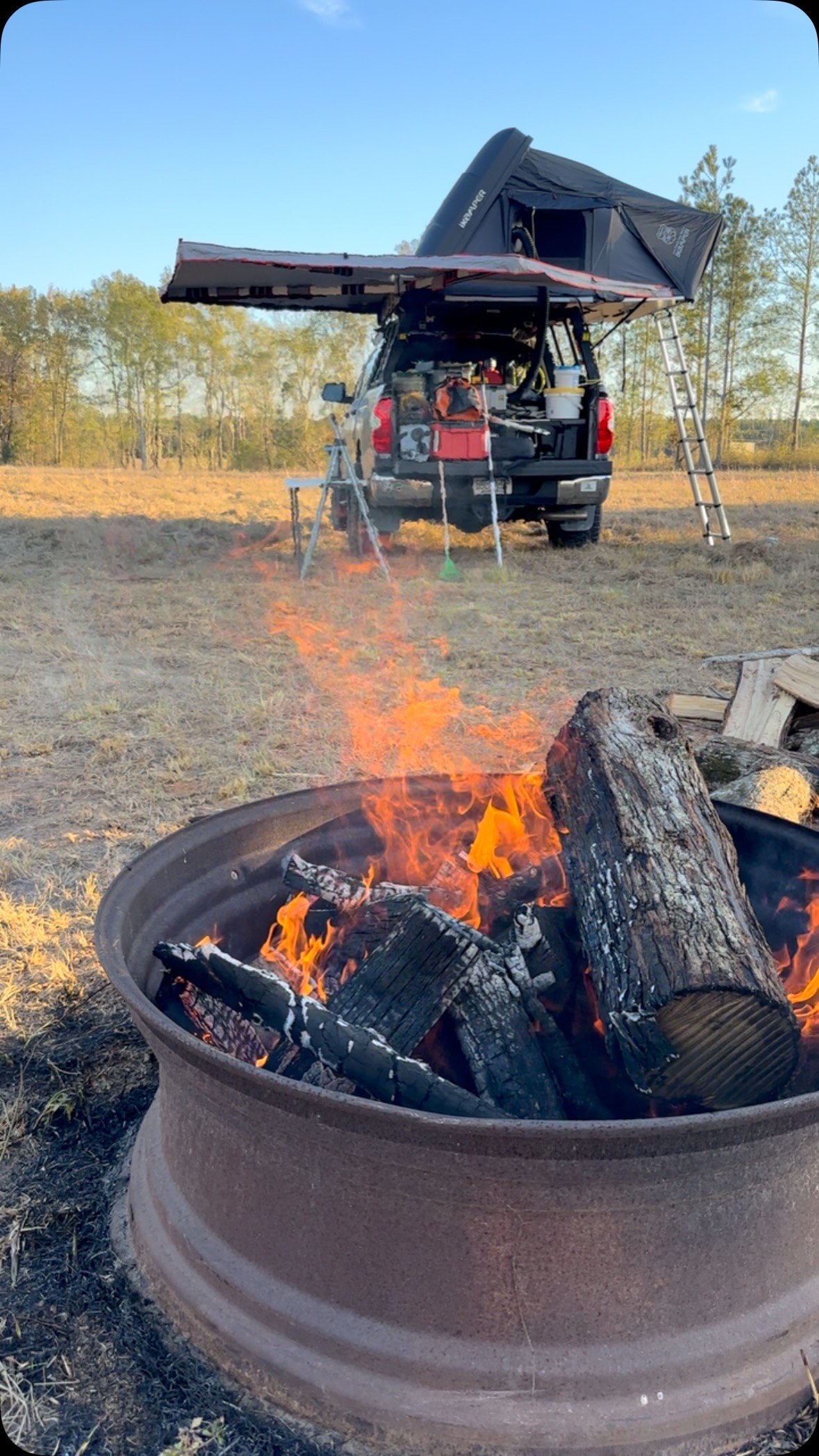 Campfire burning beside a rooftop tent at golden hour