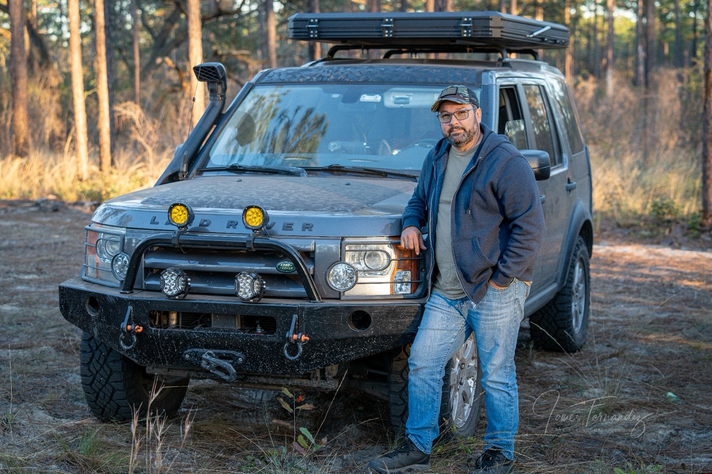 James Fernandez standing beside his Land Rover LR3 on a wooded trail